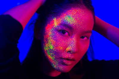 Portrait of fashionable woman with colored fluo painting on the face - Fashion model on colored background