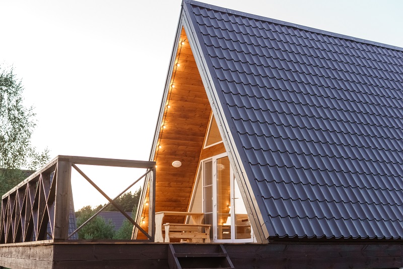 The concept of glamping and renting a chalet for weekend. Wooden house with a veranda in nature around coniferous trees.