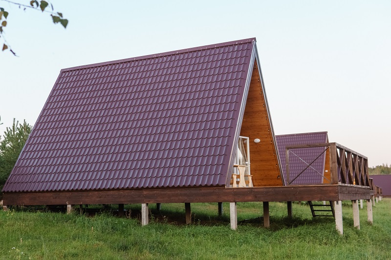 The concept of glamping and renting a chalet for weekend. Wooden house with a veranda in nature around coniferous trees.